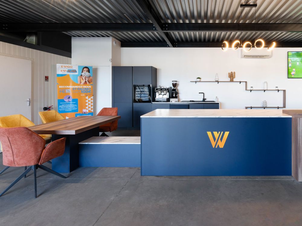 cuisine bleu, espace détente client chaleureux et machine à café à grains aux couleurs d'ewigo franchise, au sol un parquet bois rénovation tertiaire cestas